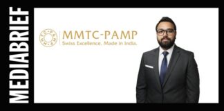 Businessman in a dark suit standing beside the MMTC-PAMP logo on a white background.