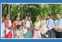 Aahwahan Foundation launches Assam Flood Relief 2026 mission Community health volunteers distribute supplies to a line of men, women, and children in a forested area, with MEDIABRIEF branding on the left.
