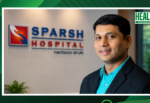 SPARSH Hospitals appoints Kalappa K.B. as Group Chief Human Resources Officer Professional portrait of a man in a blue shirt and dark suit standing in front of a Sparsh Hospital sign, with a Health Brief logo in the corner.